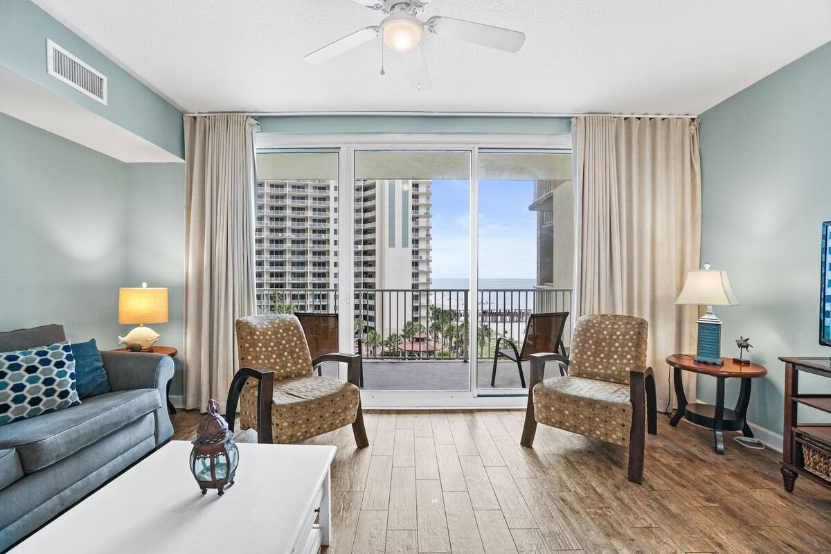 A living room with a sofa, two armchairs, a coffee table, and a balcony with a view of high-rise buildings.