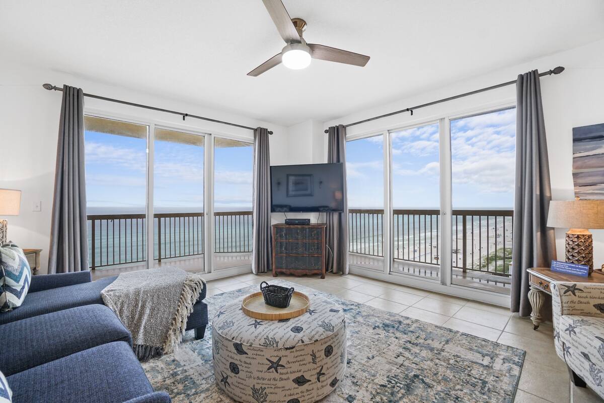 A spacious living room with a large balcony, a ceiling fan, and a television.