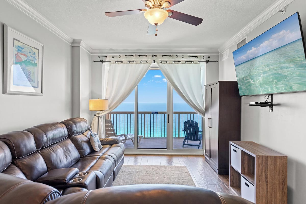 A living room with a leather sofa, a television, and a view of the ocean through a sliding door.