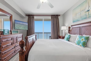 A hotel room with a bed, a dresser, a television, a painting, and a balcony with curtains.