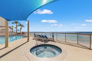 A pool area with a hot tub, lounge chairs, and a view of the ocean.