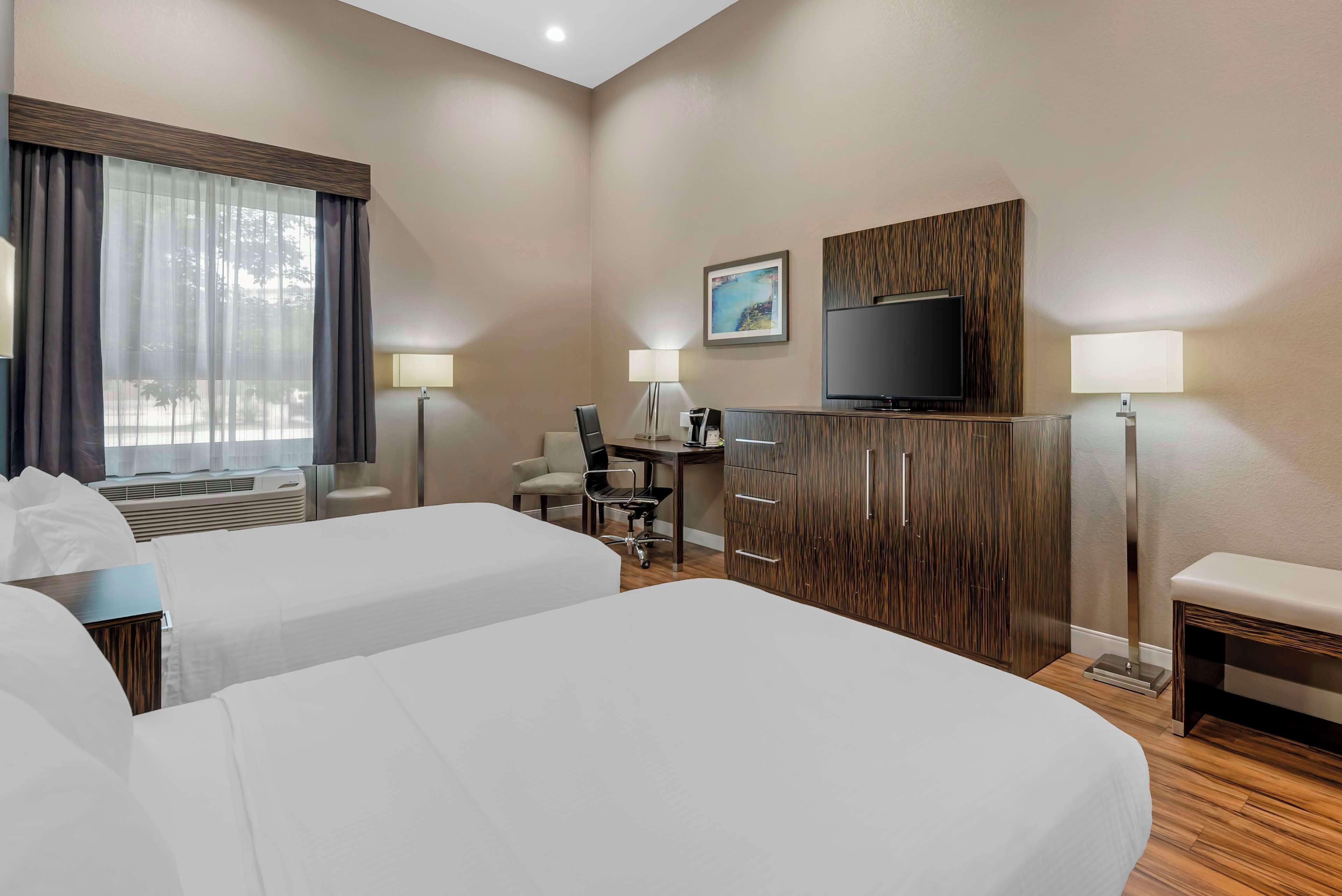 A hotel room with two beds, a desk, a chair, a TV, and a window with curtains.