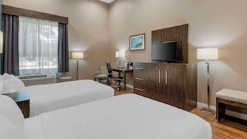 A hotel room with two beds, a desk, a chair, a TV, and a window with curtains.