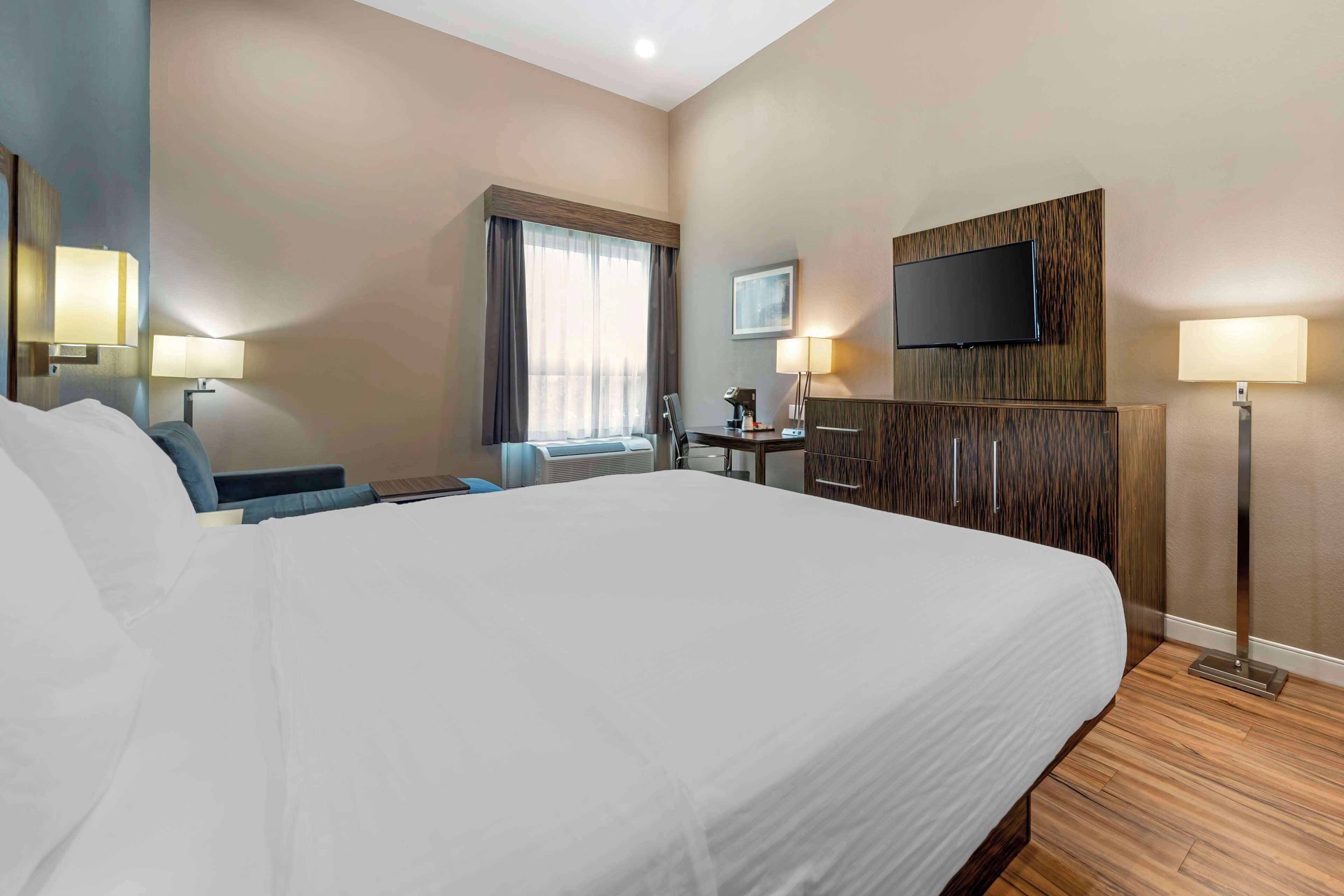 Een hotelkamer met een groot bed, een bureau met stoel, een flatscreen-televisie aan de muur en een raam met gordijnen.