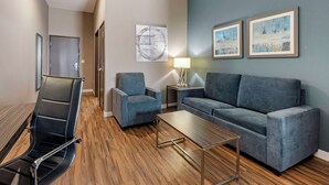 A modern living room with a sofa, armchair, and a coffee table. There is a door and a lamp on a side table. - Best Western Plus Pflugerville (Pflugerville)