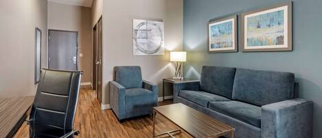 Una sala de estar moderna con un sofá, un sillón y una mesa de centro. Hay una puerta y una lámpara sobre una mesita.