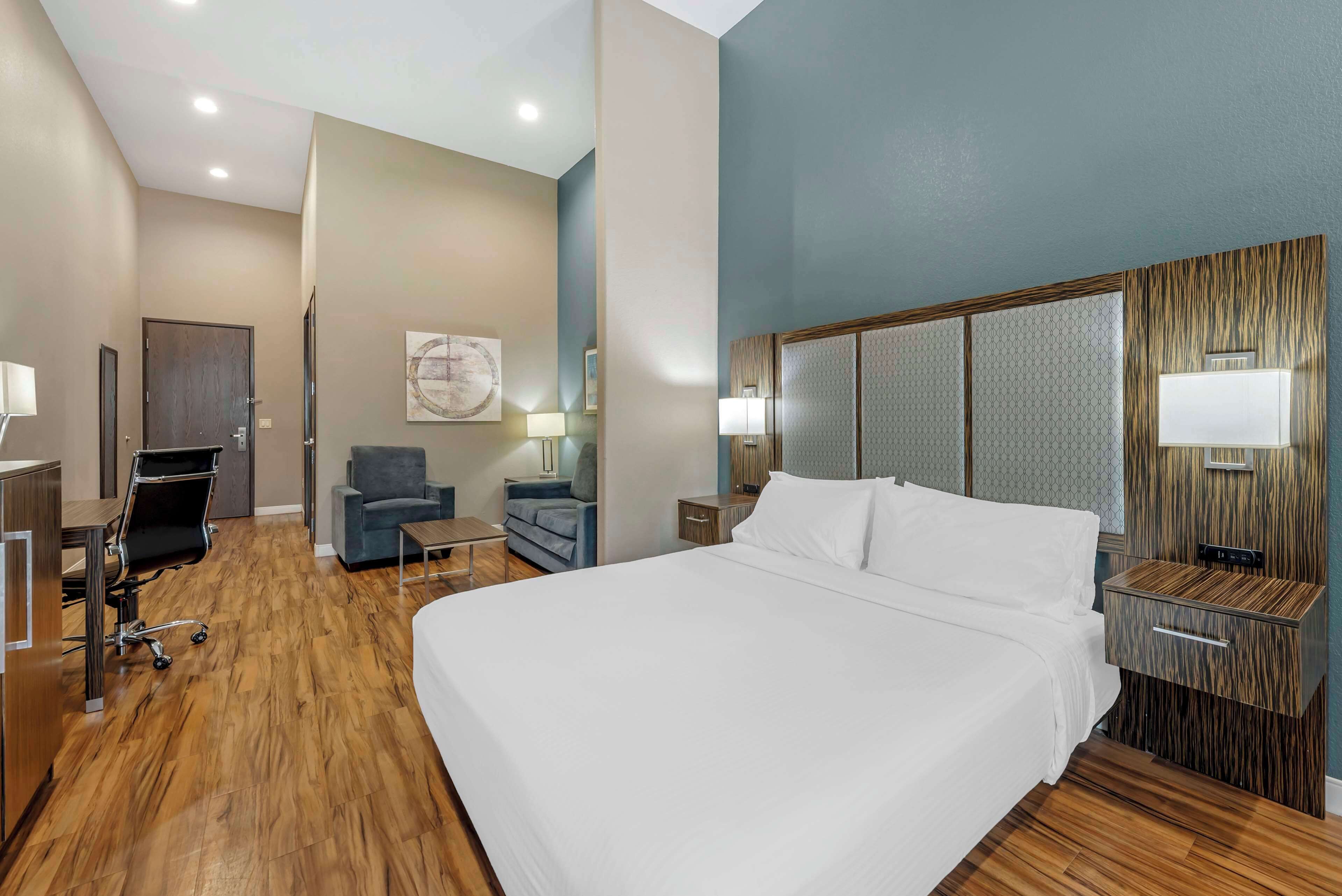 Una habitación de hotel con una cama grande, un escritorio con silla, un pequeño sofá y una mesita de noche con lámpara.