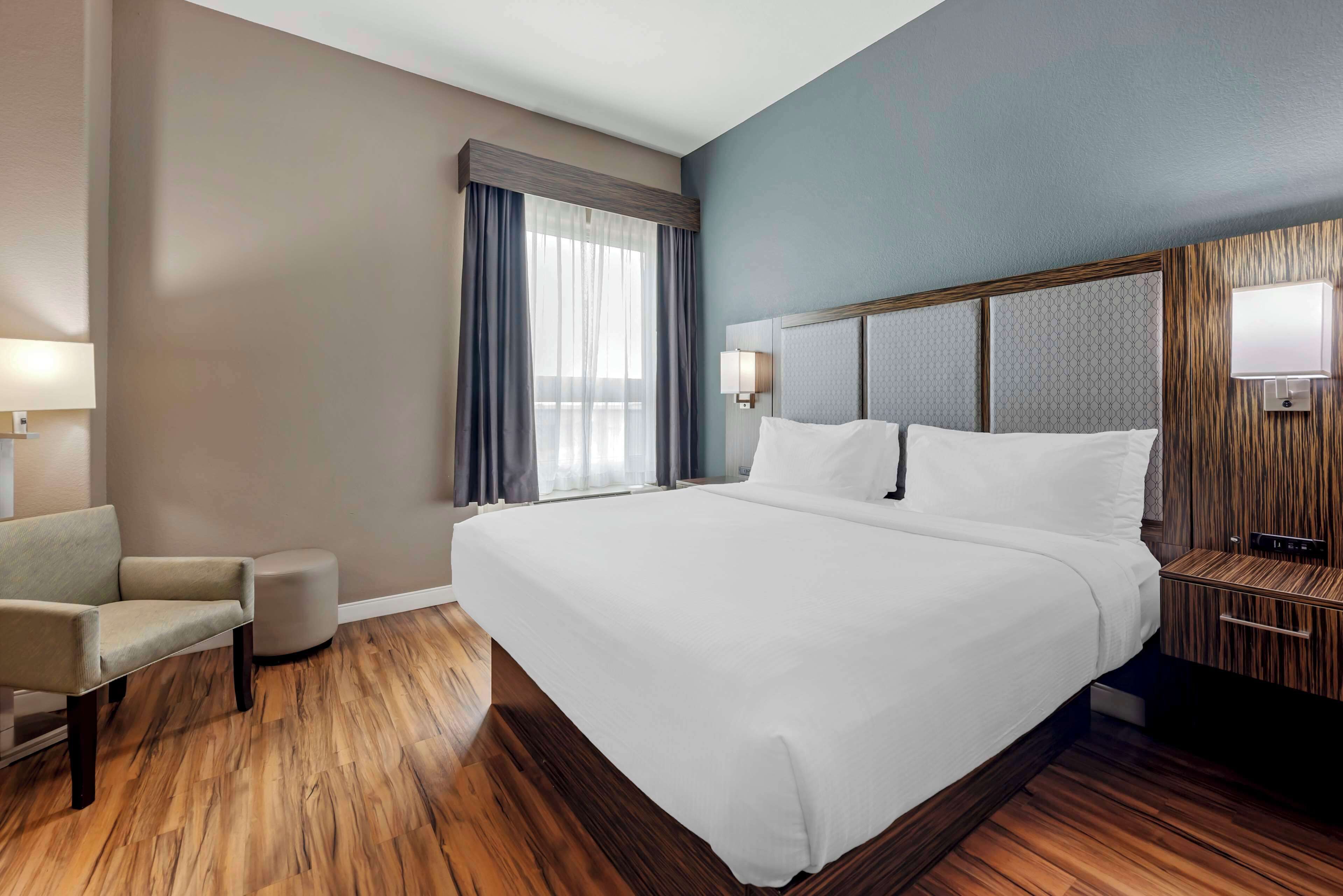 Ein Hotelzimmer mit einem großen Bett, einem Sessel, einem Nachttisch und einem Fenster mit Vorhängen.