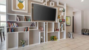 A modern living room with a large flat-screen TV, built-in bookshelves, decorative items, and a patterned sofa. - Best Western Plus Pflugerville (Pflugerville)