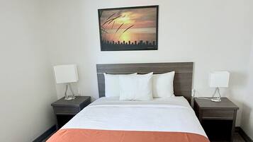 Una habitación de hotel con una cama grande, dos mesitas de noche, un buró, un cuadro en la pared y un suelo de color claro.