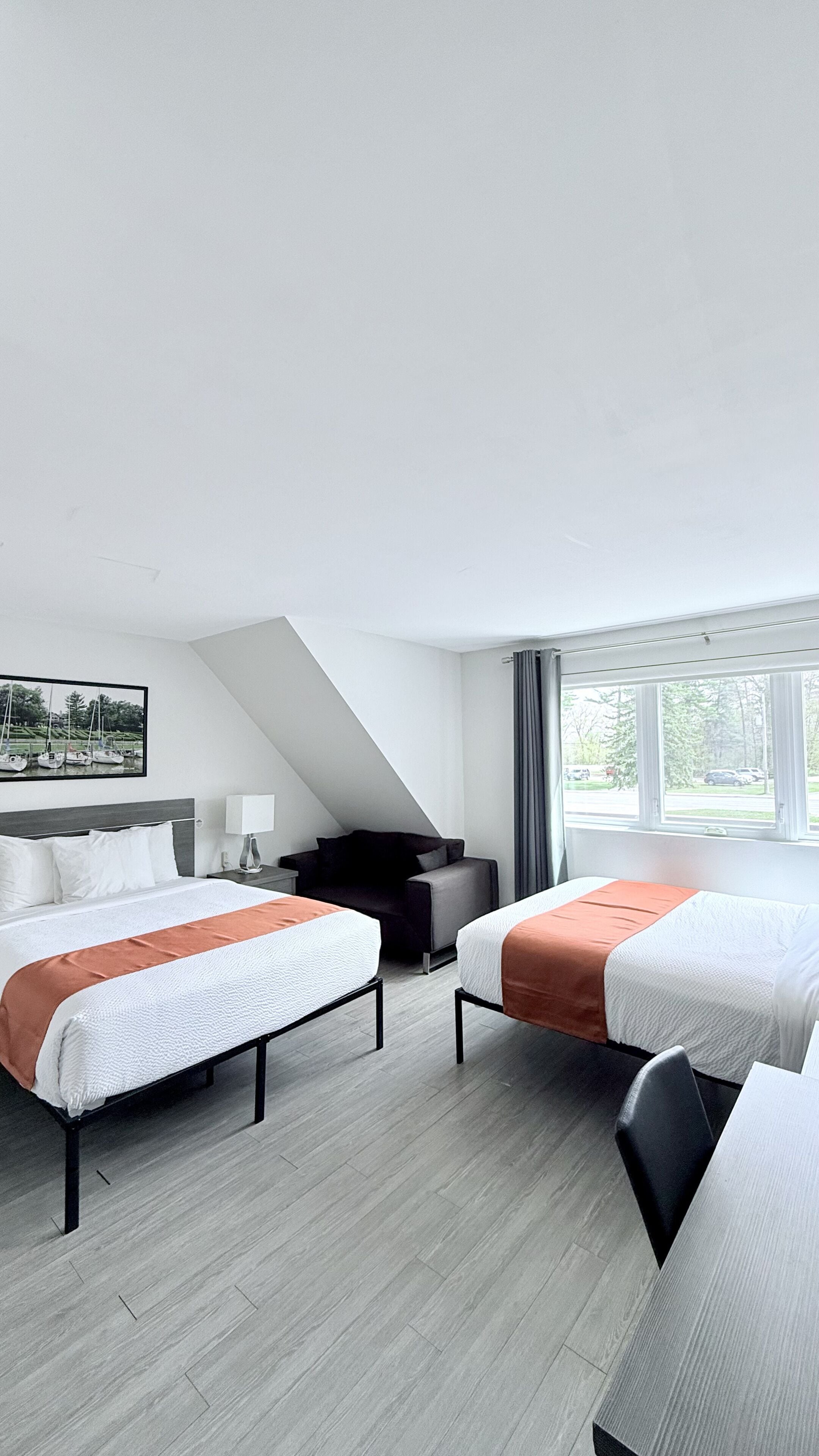 A hotel room with two beds, a sofa, a desk, and a large window.