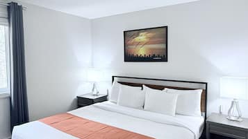 A hotel room with a large bed, two bedside tables, a nightstand, a window with curtains, and a cityscape painting on the wall.
