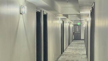 A long, narrow hotel corridor with carpeted floors, doors on both sides, and overhead lighting.