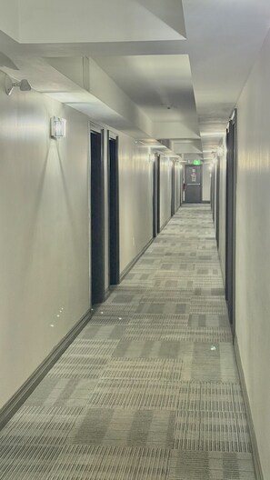 A long, narrow hotel corridor with carpeted floors, doors on both sides, and overhead lighting. - Amber Hotel (Lambton Shores)