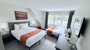 A hotel room with a bed, bedside tables, a desk, a TV, and a window with curtains. - Amber Hotel (Lambton Shores)