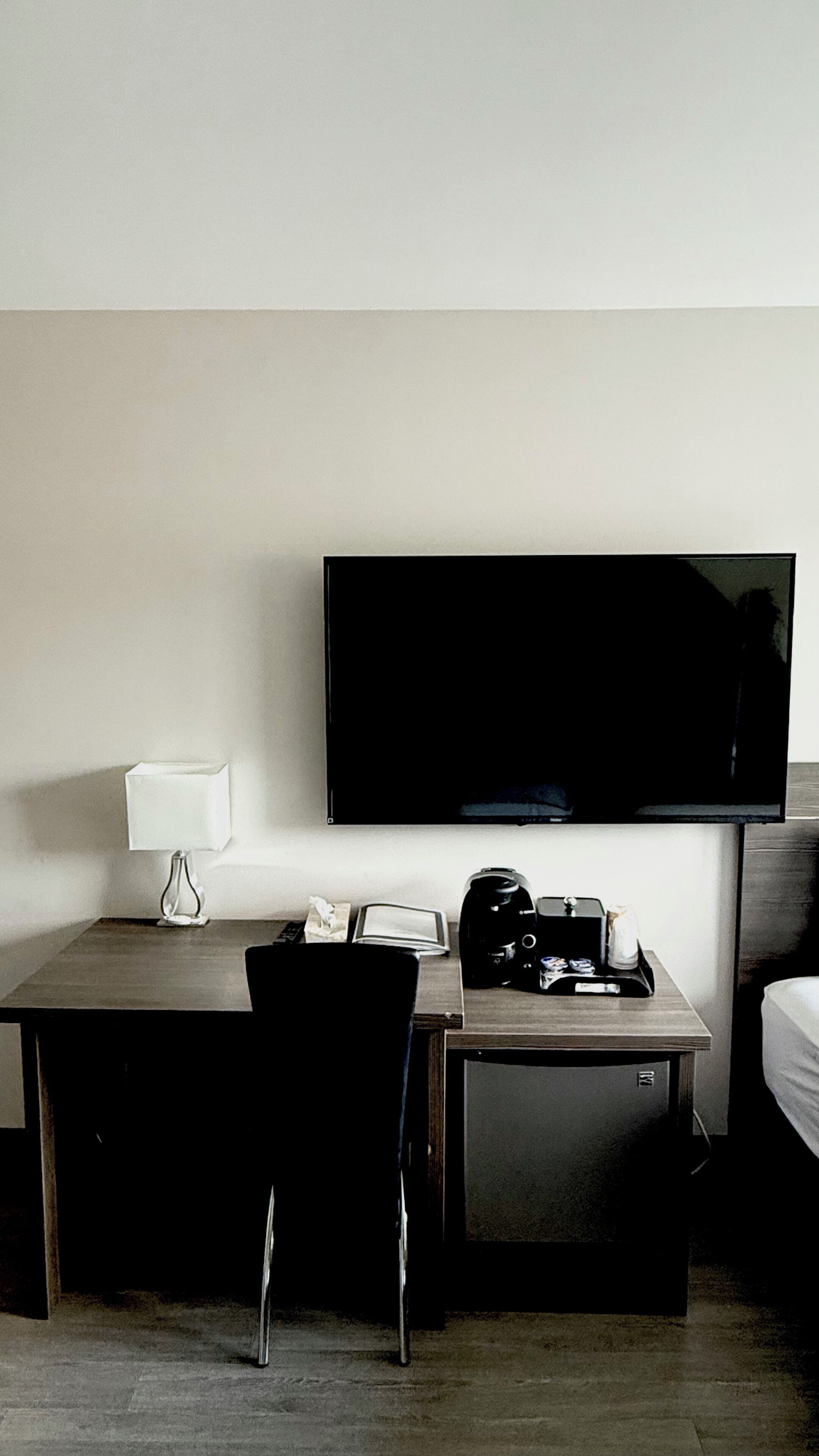A hotel room with a bed, a desk with a chair, a television, a lamp, and a coffee maker.