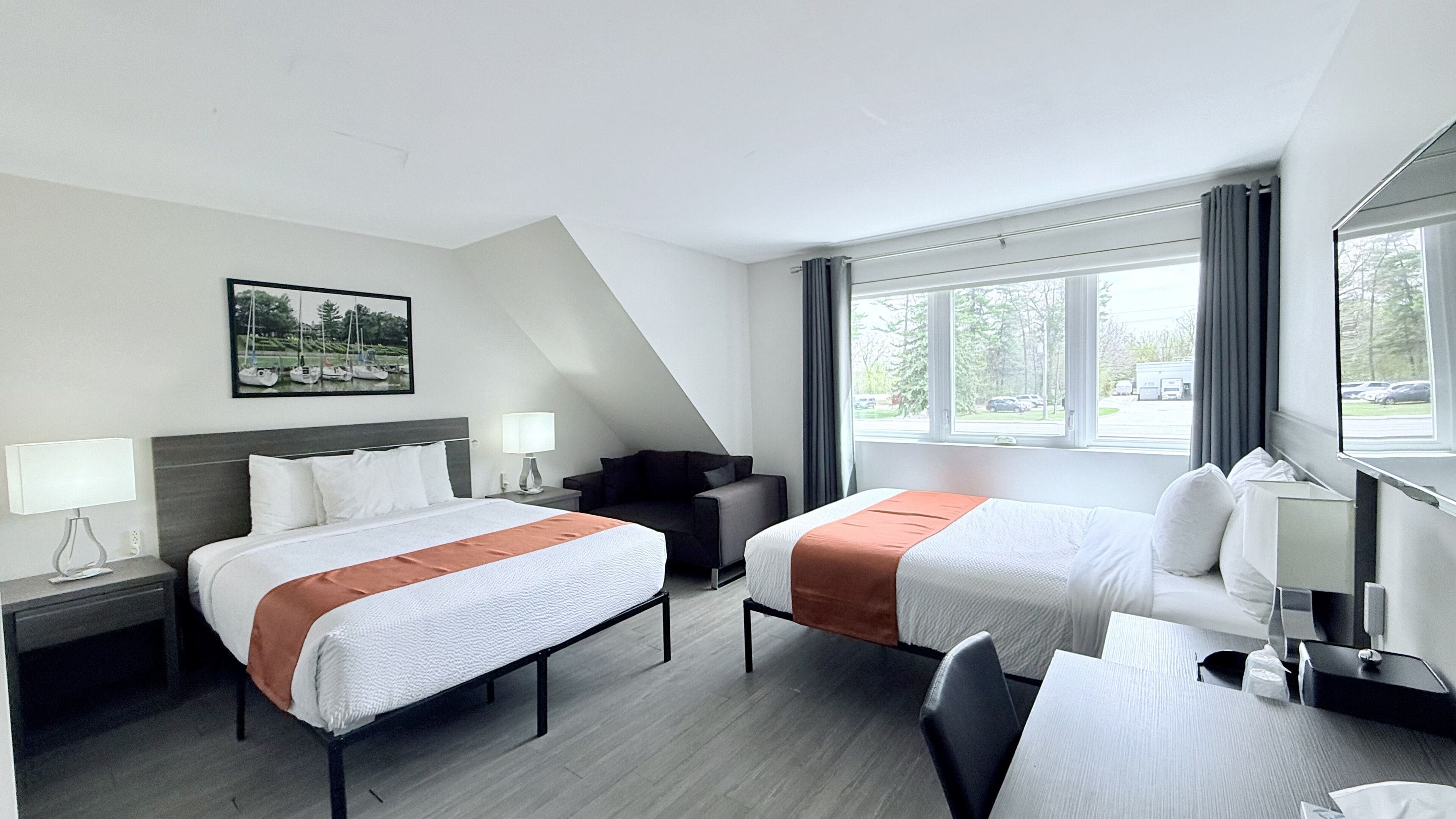 Habitación de hotel con dos camas, un escritorio, una silla, un sofá y un ventanal grande.