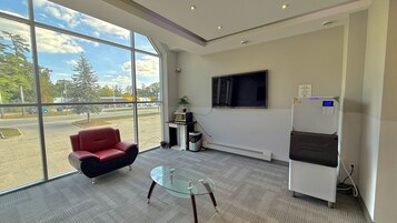 Un espacio de oficina moderno con un gran ventanal, una silla roja, una mesa de vidrio, un microondas y un refrigerador.