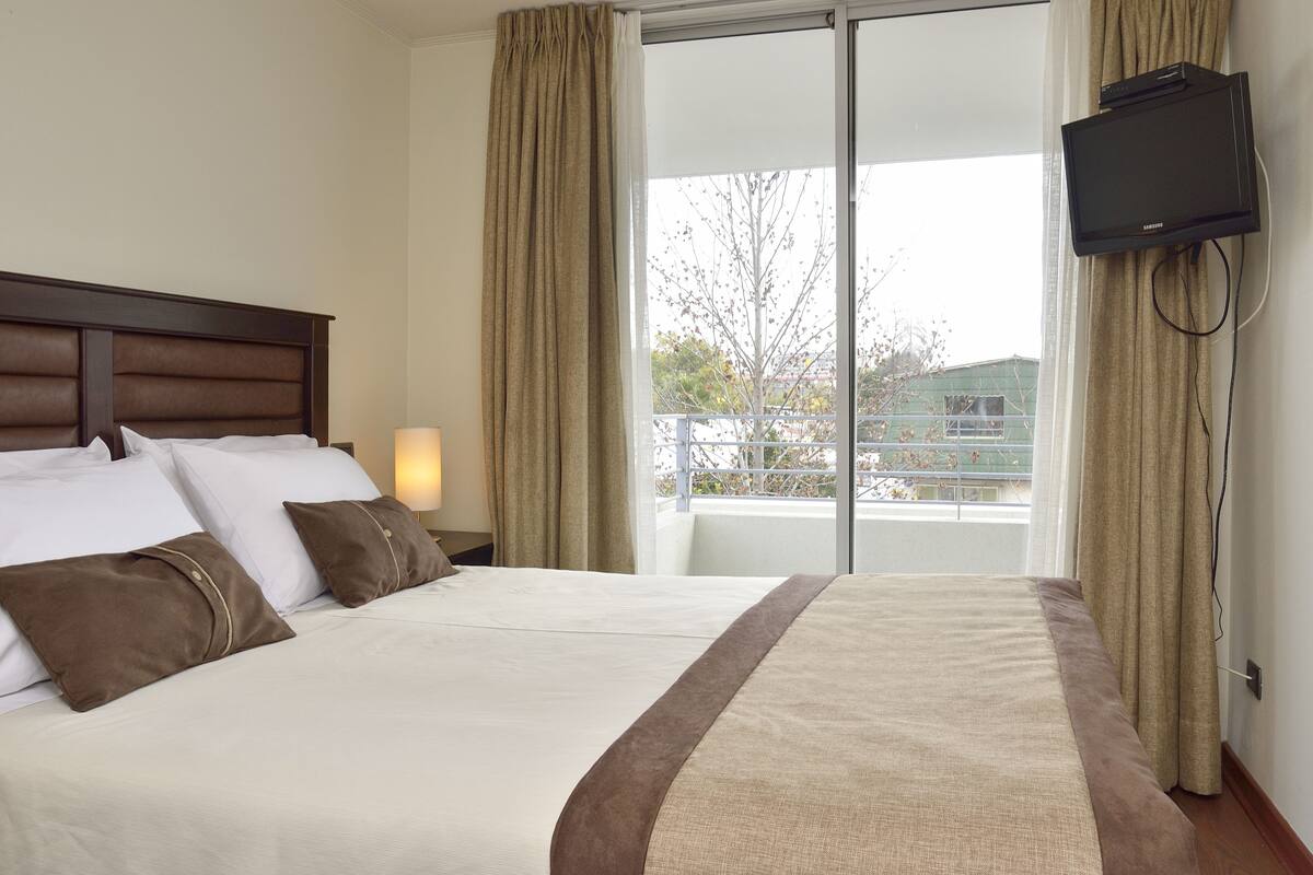 Habitación de hotel con una cama grande, un televisor montado en la pared y vista al balcón exterior.