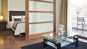 Quarto de hotel com uma cama, uma mesa de centro de vidro, uma cadeira e vista para o exterior.