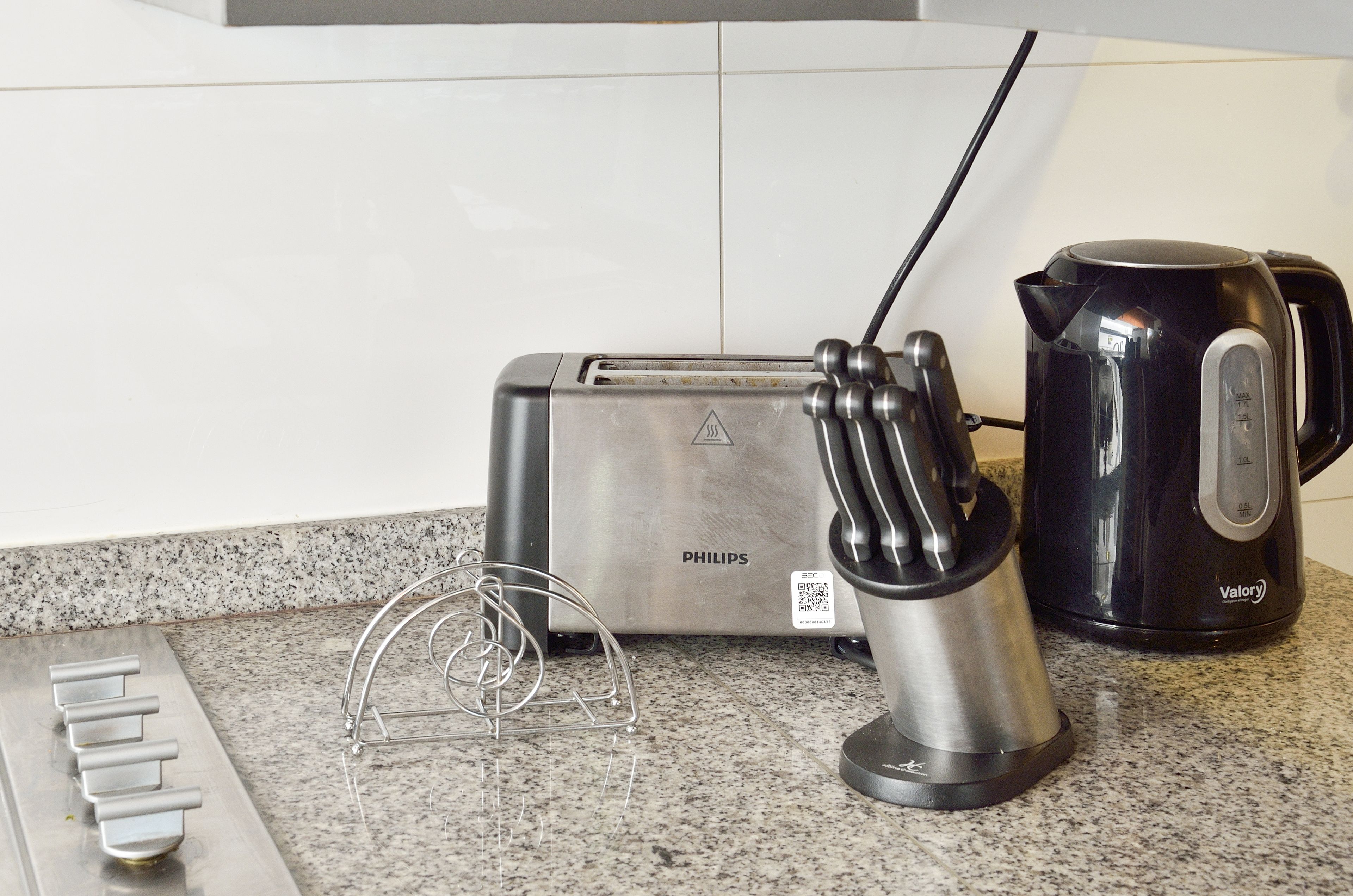 Een keuken met een Philips broodrooster, een zwarte Valory koffiezetapparaat en een metalen houder voor keukengerei op een granieten aanrecht.