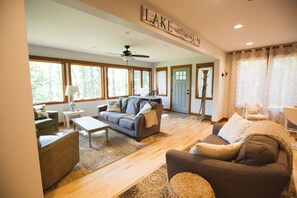 A spacious living room with a ceiling fan, large windows, and a sign that reads "LAKE".