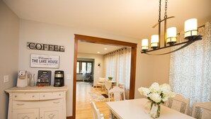A dining area with a white table, chairs, and a chandelier. There is a sign on the wall that reads "Welcome to THE LAKE HOUSE."