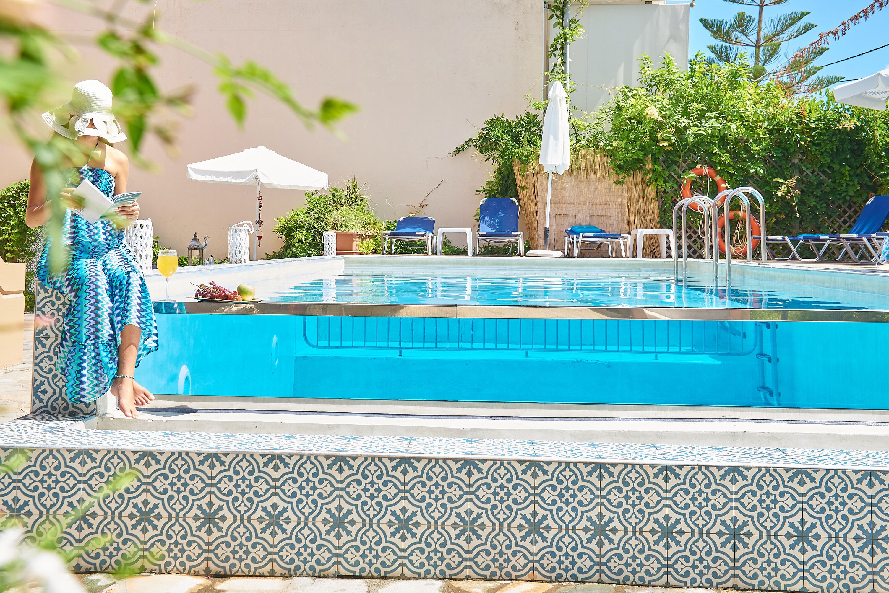 A swimming pool with tiled edges, lounge chairs, and umbrellas.