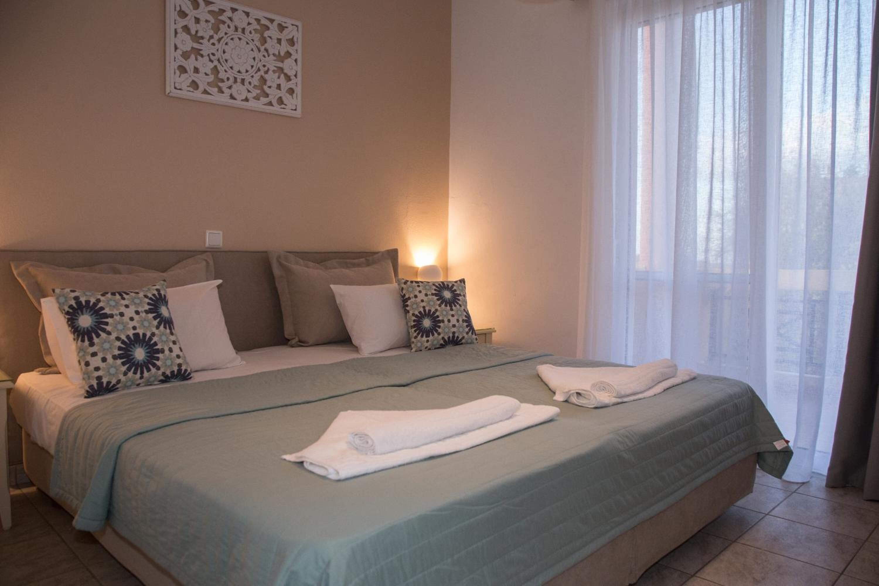 Habitación de hotel con una cama grande, dos lámparas de noche, un adorno en la pared y una ventana con cortinas traslúcidas.