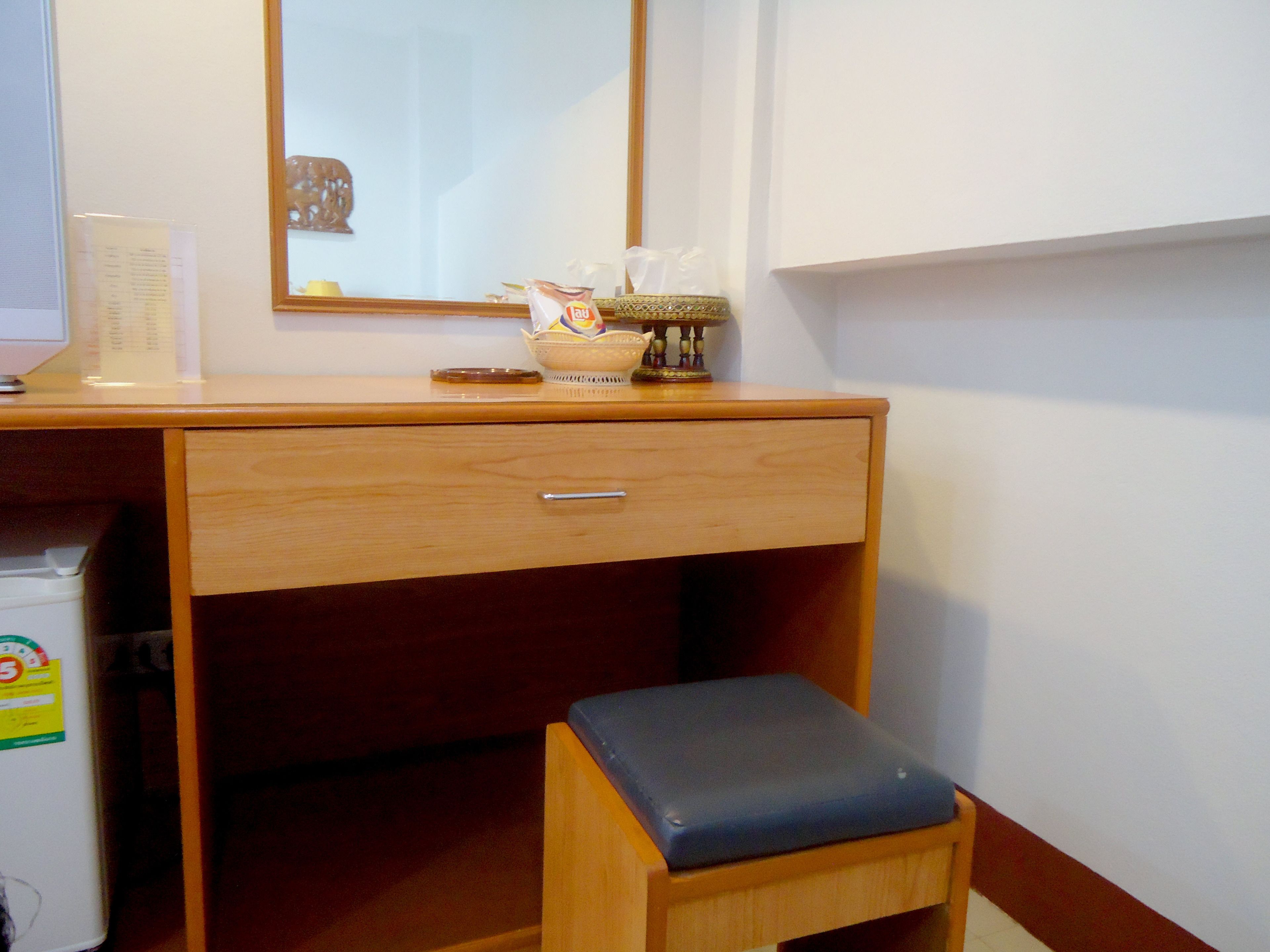 Un escritorio de madera con un cajón, un taburete pequeño con asiento azul y un espejo en la pared.