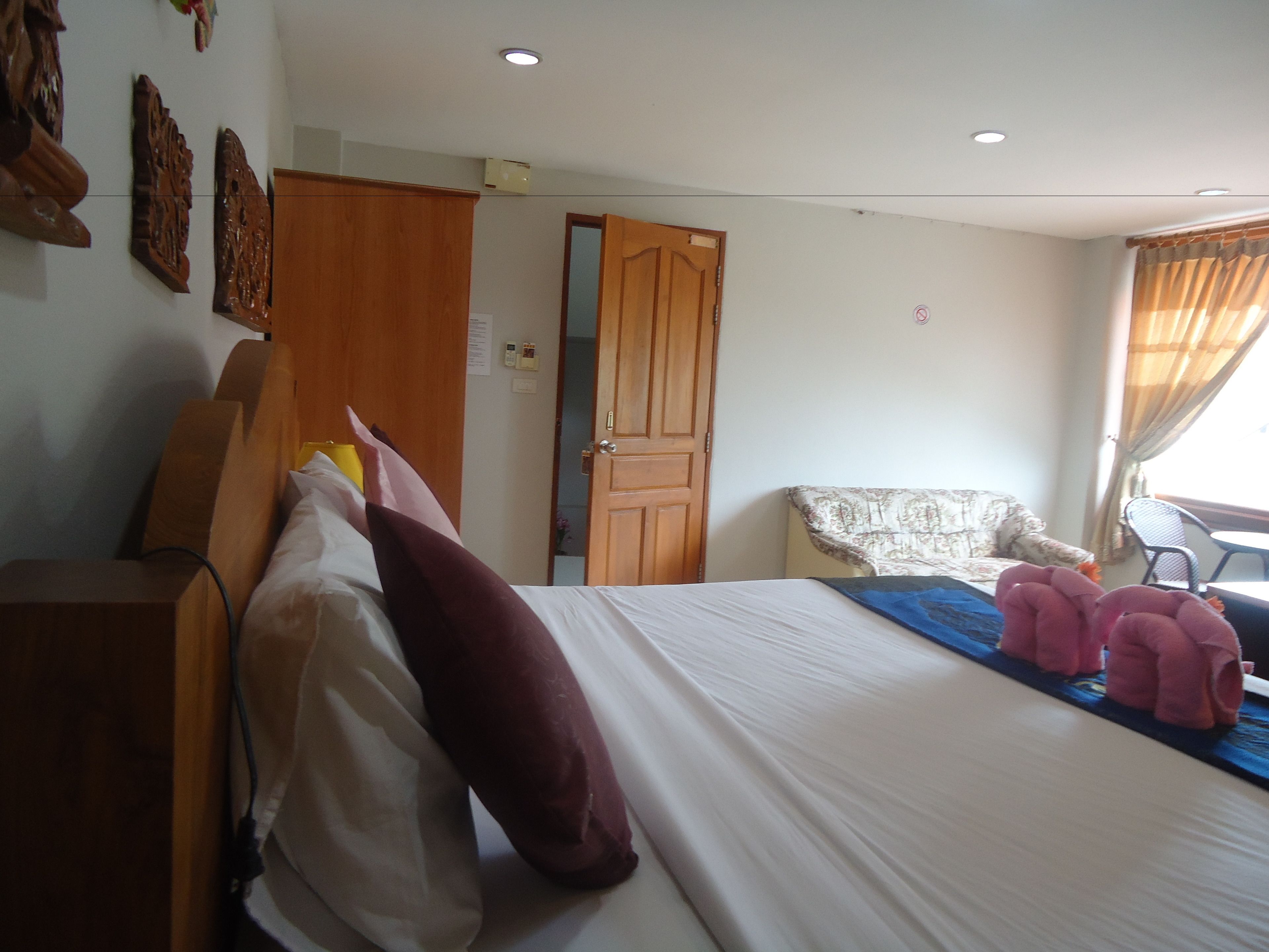 Una habitación de hotel con cama, armario de madera, una silla y ventana con cortinas.
