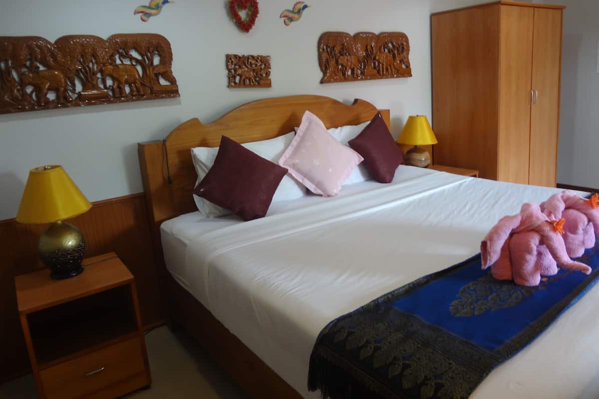 Un dormitorio con cabecera de madera, una cama con ropa blanca, dos mesitas de noche con lámparas, un armario y adornos en la pared que incluyen motivos de corazón y pájaros.