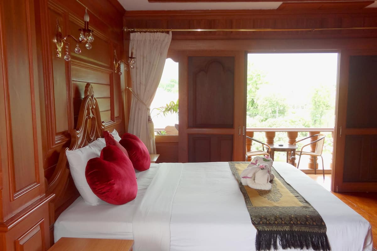 Un dormitorio con estructura de madera, una cama grande, almohadas rojas, una colcha blanca y un cojín decorativo.