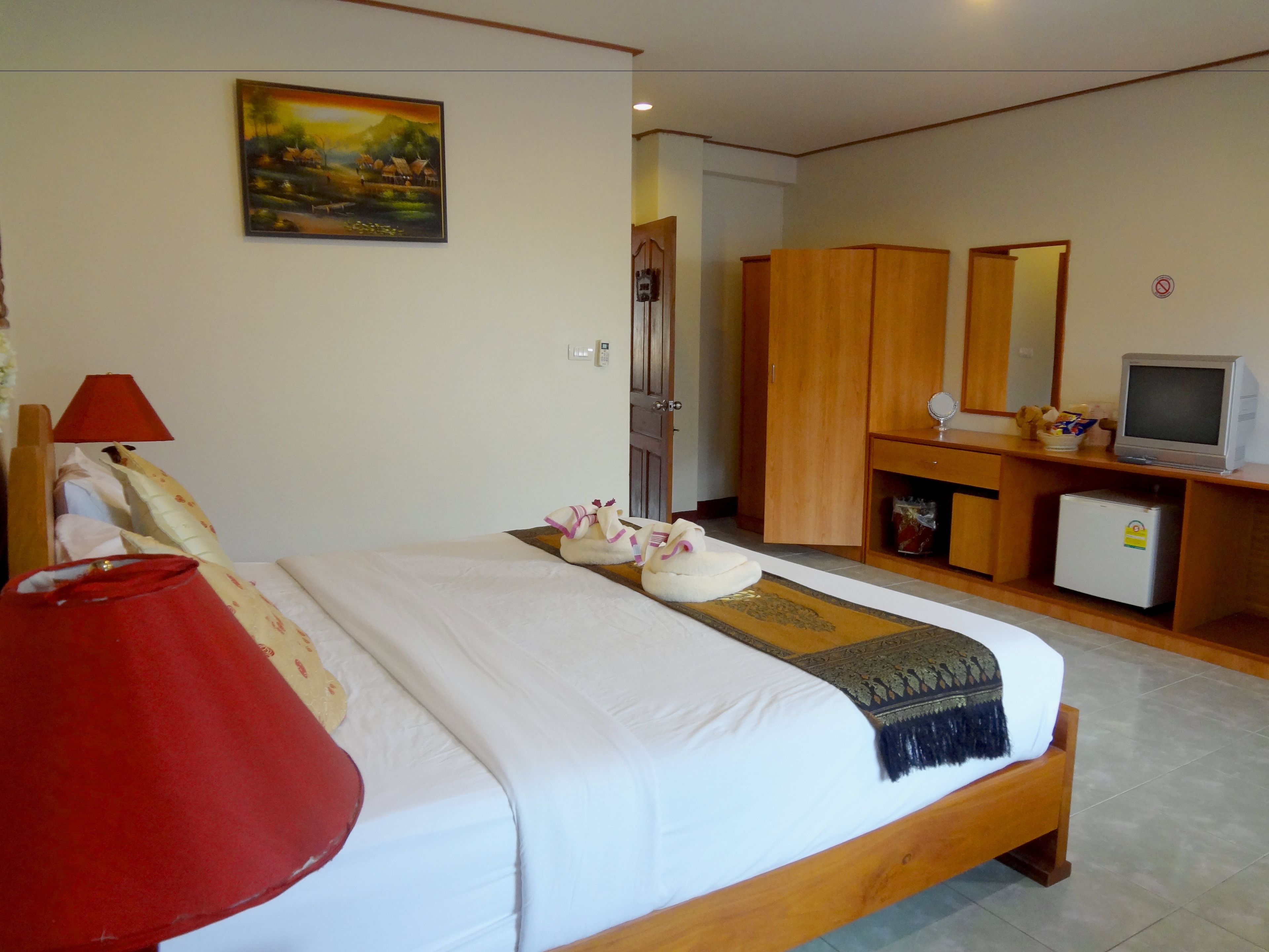 A hotel room with a bed, a desk with a computer, a TV, and a painting on the wall.
