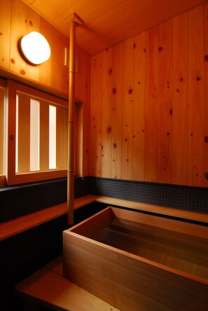 A wooden interior with a large wooden bathtub, a window with vertical blinds, and a tiled wall. - Nenoyu Taizansou (Izu)