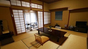 Et traditionelt japansk rum med tatamimåtter, et lavt bord med puder, et fjernsyn og skydedøre.