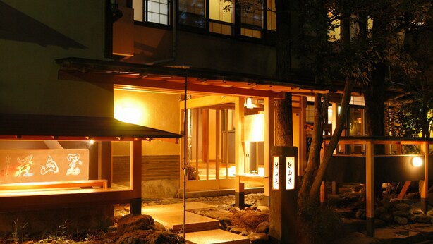 En traditionel japansk bygning med trækonstruktion, oplyst interiør og stensætninger, der fører op til indgangen.