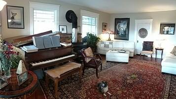 Ett vardagsrum med ett piano, en vit soffa, en mönstrad matta och en hund.