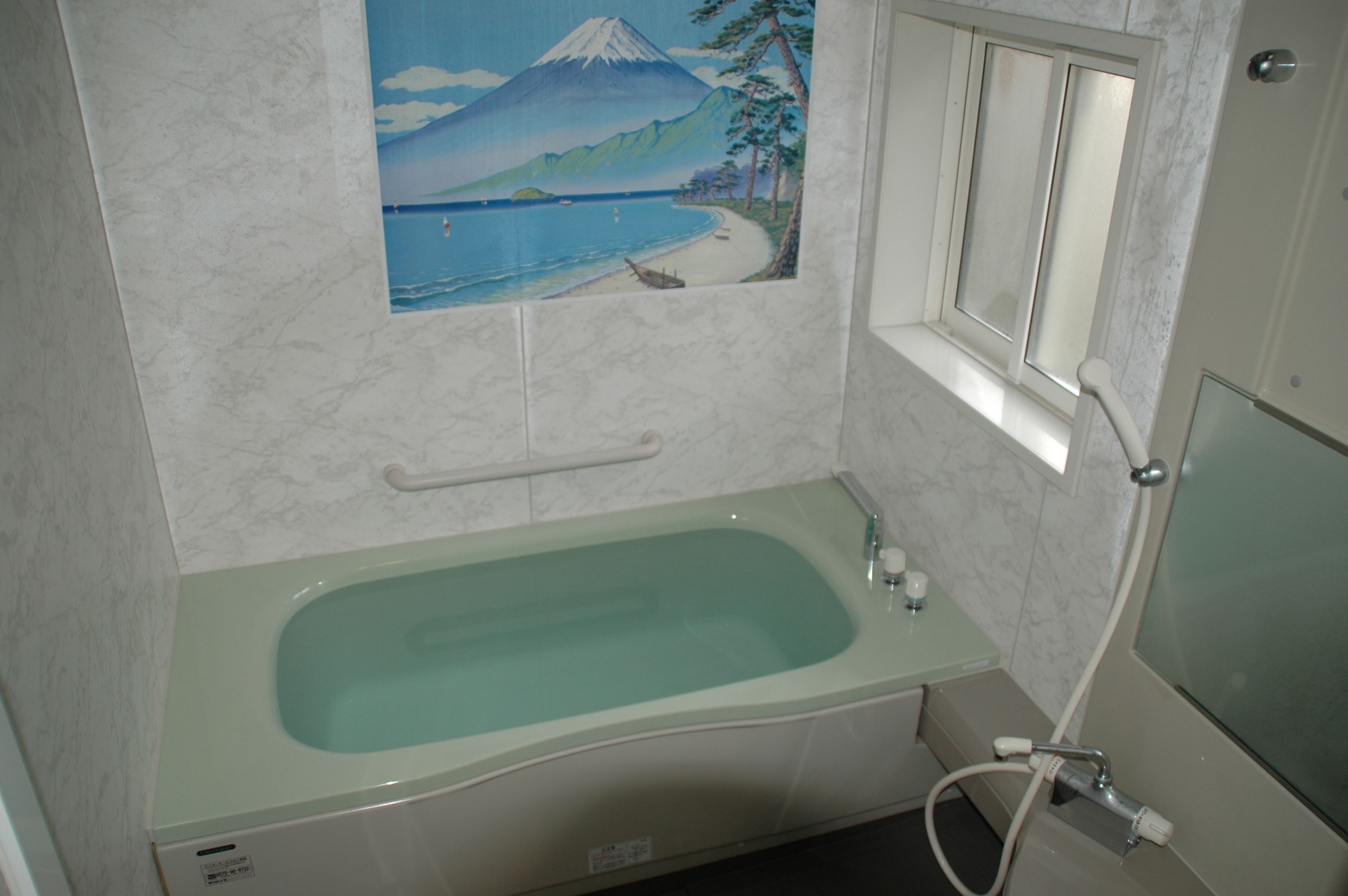 A bathroom with a bathtub, a window with a view of a mountain and beach, and a mirror.