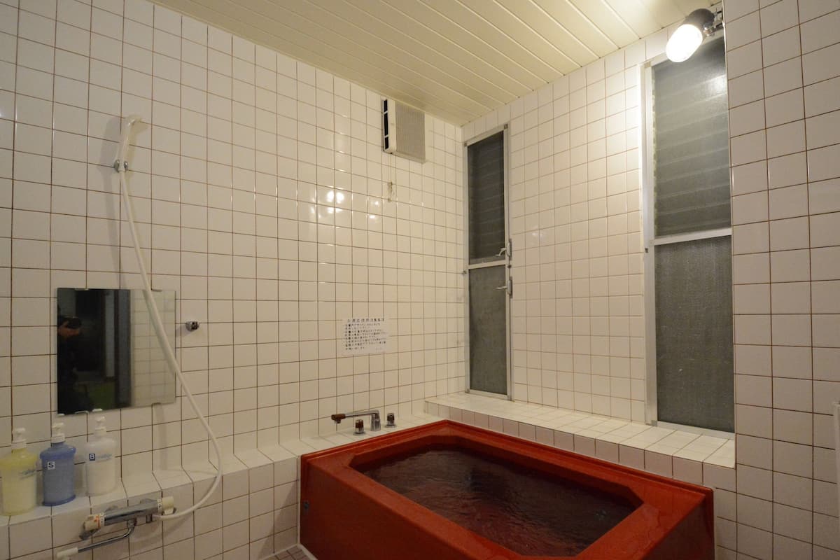 Ein Badezimmer mit weiß gefliesten Wänden, einer roten Badewanne, einem Fenster und einem Spiegel.
