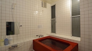 Un baño con paredes de azulejos blancos, una bañera roja, un ventanal y un espejo.
