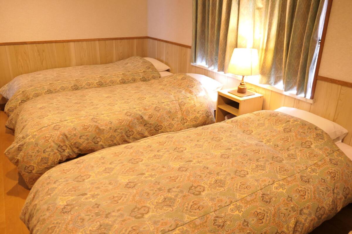 Ein Hotelzimmer mit zwei Betten, einem Nachttisch mit Lampe und einem Fenster mit Vorhängen.