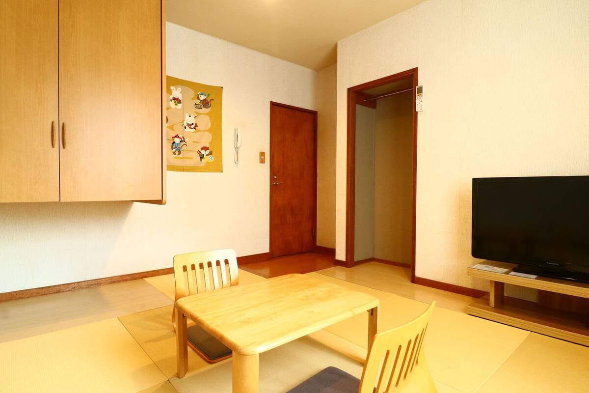 Ein Zimmer mit Holzschrank, Fernseher, Esstisch und Stühlen sowie einer Tür.