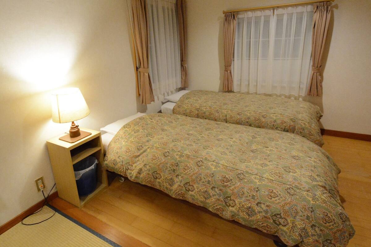 Ein Schlafzimmer mit zwei Betten, einem Nachttisch mit Lampe und einem Fenster mit Vorhängen.