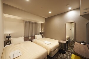 A hotel room with two beds, a bedside table with a lamp, a small round table, and a mirror.