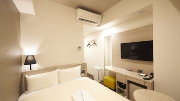 Habitación de hotel con cama, lámpara de noche, aire acondicionado, televisor, escritorio y espejo.