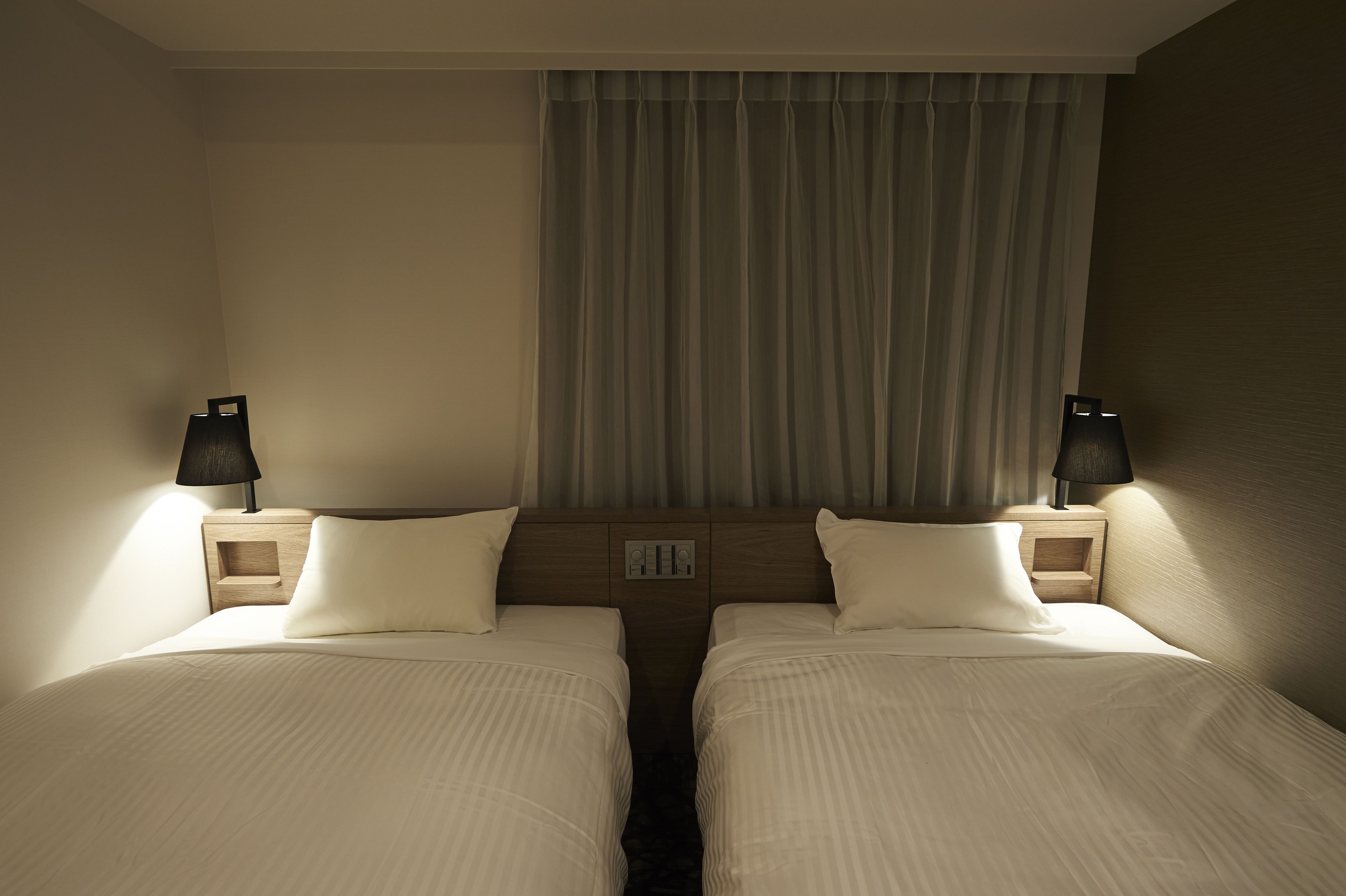 A hotel room with two beds, a wooden headboard, bedside lamps, and a window with curtains.