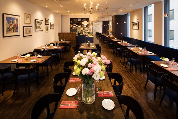 Un restaurant doté de nombreuses tables, chacune étant dressée avec des assiettes, des couverts et un centre de table composé de fleurs.