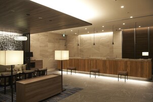 A modern lobby with a reception desk, seating area, and a large chandelier.