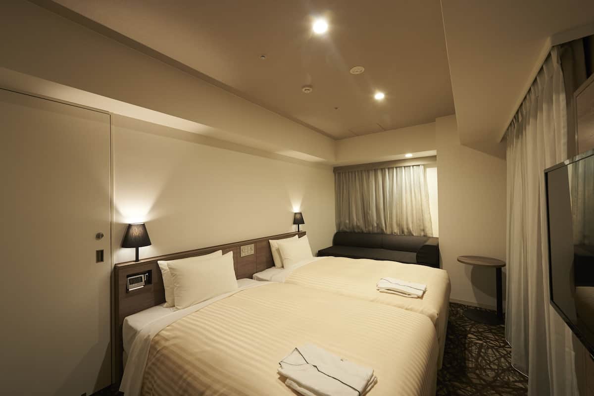 A hotel room with two beds, a bedside table, a lamp, a small round table, and a large mirror.